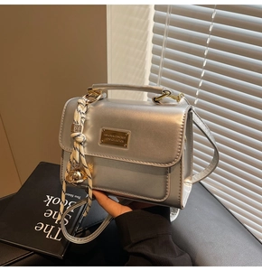 Detail of silver metallic square handbag with gold logo plate and bell charm
