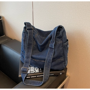 Detail of dark blue washed denim shoulder bag with side pockets on a black bench