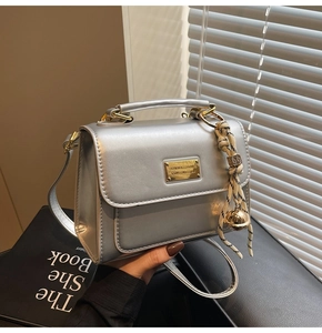 Detail view of silver crossbody bag with golden buckle and decorative bell charm