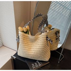 Detail of straw woven tote with black and white striped ribbon handle and bow accent