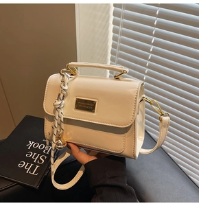 Detail view of cream-white square handbag with golden hardware and decorative charms