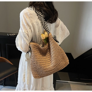Detail of straw woven tote bag with black and white striped scarf shoulder strap