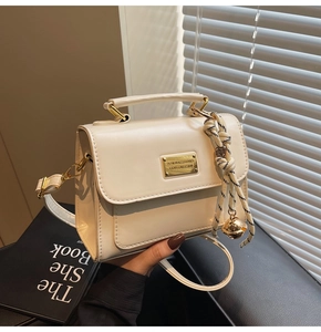 Detail of cream white crossbody bag with gold hardware and woven rope charm decor