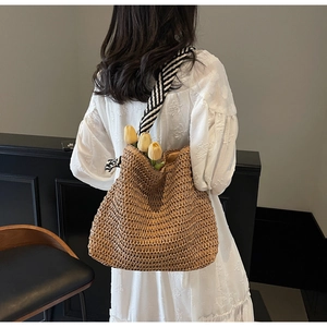Detail of straw shoulder bag with black and white striped strap on white dress