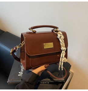 Close-up of brown glossy crossbody bag with gold metal handle and logo plate detail