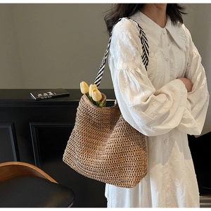 Detail of woven straw tote bag featuring contrast black and white striped webbing handles