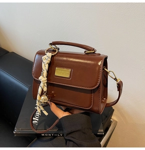 Detail of glossy brown mini crossbody bag with gold metal plate and bell charm