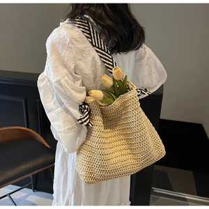 Detailed close-up of straw woven tote with striped shoulder straps on a model