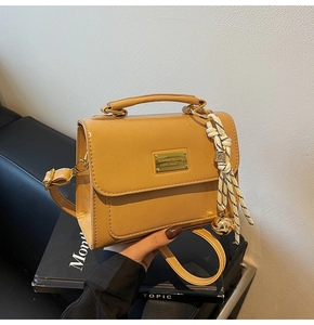 Detail of caramel crossbody bag with golden plaque and decorative braided rope charm