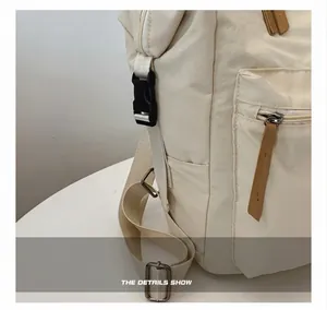 Detalle de la mochila de nailon crema con hebilla lateral negra y tirador de cuero marrón