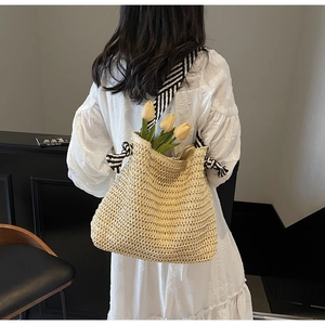 Detailed close-up of a beige straw tote bag with black and white striped canvas strap