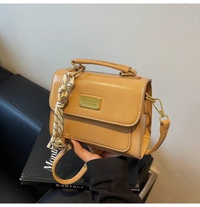 Detail of camel leather crossbody bag featuring gold hardware and striped charm