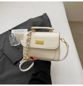 Detail of a chic cream small square bag with golden hardware and fashion charm