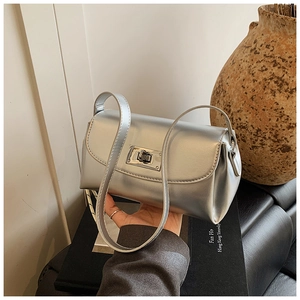 Détail d'un sac baguette argenté métallique avec fermoir rotatif sur décor de livre