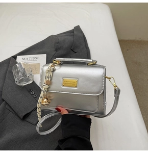 Detail of silver metallic square handbag with gold logo plate and striped ribbon charm