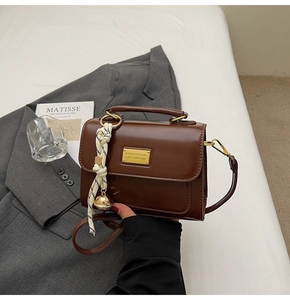 Detail of a vintage brown crossbody bag with gold bell pendant and woven rope charm