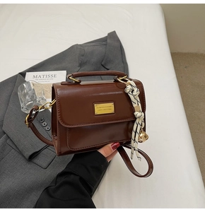 Detail view of brown glossy leather crossbody bag with gold hardware and bell charm