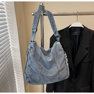 Detail view of denim tote bag with metal zipper and adjustable strap on a hanger