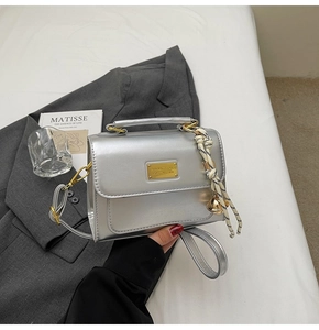 Detailed shot of a silver metallic crossbody bag with a braided charm and gold accents