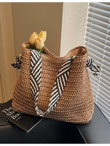 Natural straw tote bag with black-white striped shoulder strap and bow on a sofa