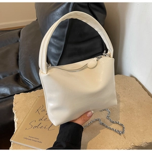 Macro detail of creamy white leather pillow bag with silver chain on stone base