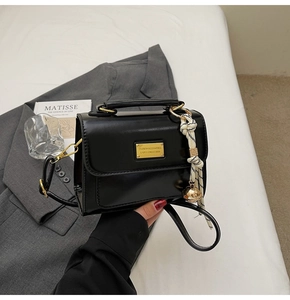 Detail of black glossy handbag with gold metal plate and woven bell charm accessory