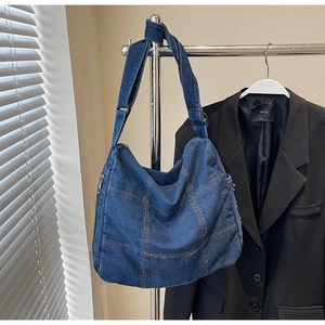 Detail of blue denim hobo bag featuring contrast orange stitching and side zipper pocket