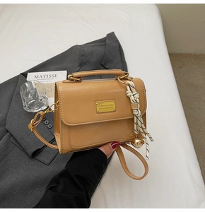 Detail of retro tan shoulder bag with gold metal plate and striped rope tassel