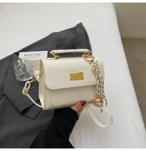 Close-up of cream crossbody bag with gold plaque and woven knot charm on a grey suit