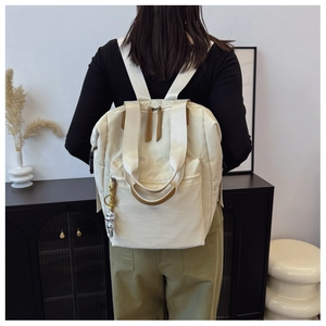 Mochila de lona beige con detalles de cuero marrón y un tierno colgante de oso plateado