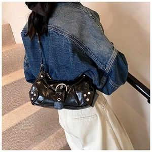 Detail of black wrinkled patent leather shoulder bag with silver buckle and metal studs