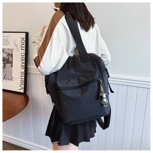 Detalle de la mochila de nailon negro con colgante de oso y hebilla lateral en modelo