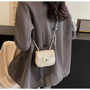 Close-up of cream quilted chain bag with V-pattern stitching and silver turn-lock closure