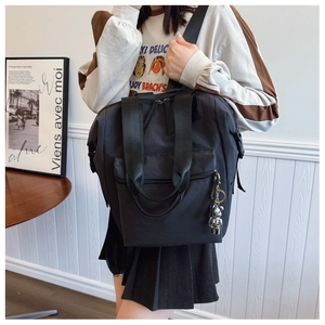 Detalle de mochila de nailon negro con asas dobles, colgante de oso y bolsillo con cremallera