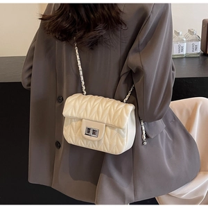 Detail of off-white quilted chain bag with silver twist lock worn over a grey blazer