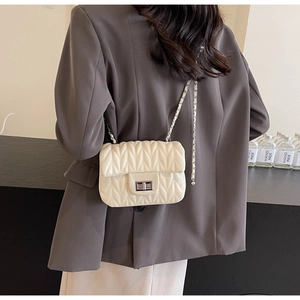Close-up of off-white quilted crossbody bag with silver rotating lock and chain strap