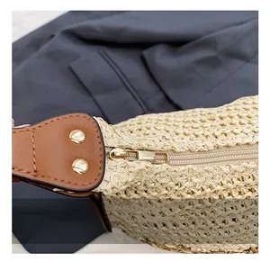 Detail of golden zipper and brown leather strap attachment on hollow woven straw tote bag