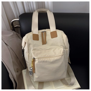Detalle de mochila de nailon blanco roto con colgante de oso plateado en escena de estilo