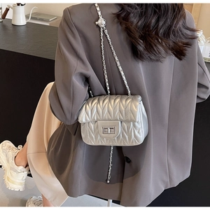 Close-up of silver quilted crossbody bag with V-stitch texture and metallic chain strap