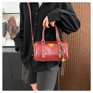 Detail of red Boston bag with gold triangular plaque and woven bell pendant on shoulder strap
