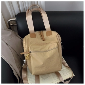 Detalle de mochila multifuncional de nailon beige y bolso tote con colgante de oso en sofá