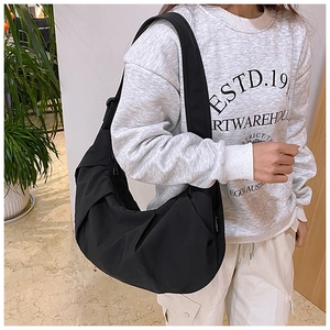 Detailed side view of black nylon crescent bag with wide strap on a model's shoulder