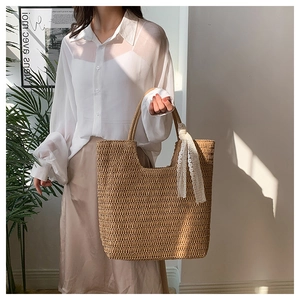 Detail of straw tote bag featuring vertical weaving texture and a white lace ribbon handle