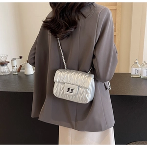 Detailed view of a silver quilted chain bag worn by a model in a stylish urban cafe setting