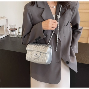 Detail of silver quilted crossbody bag with metal twist lock and chain strap on a model