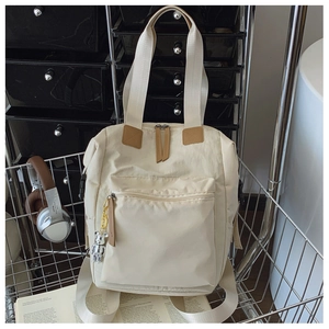 Detalle de la mochila multifuncional blanco roto con toques de cuero y oso colgante