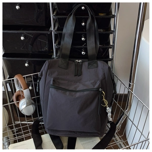 Detalle de mochila de nylon gris oscuro con colgante de astronauta y estilo urbano
