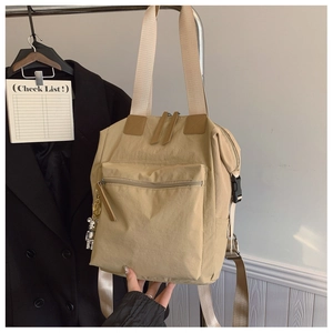 Detalle de mochila tote de nailon beige con compartimento grande y colgante de oso plateado