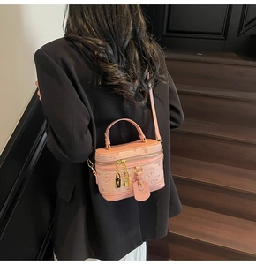 Pink embossed crossbody box bag with gold double zippers shown on a model on stairs