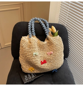 Close-up of straw woven tote bag featuring colorful knit bows and navy pleated handles